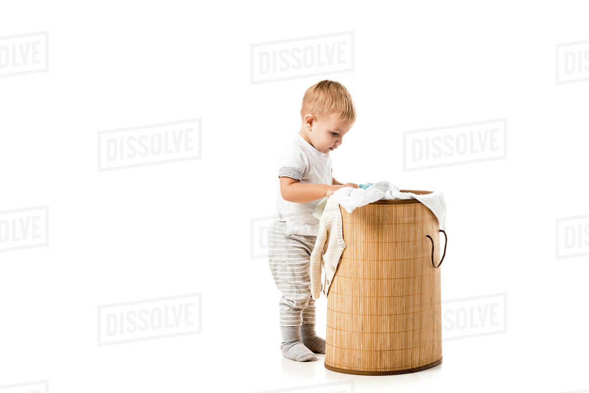 Toddler boy looking into wicker laundry basket isolated on white