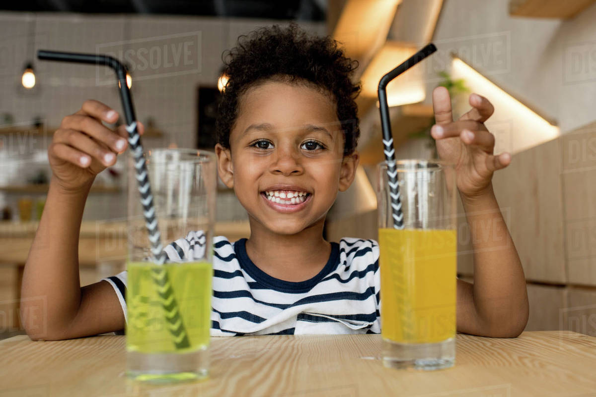 adorable african american boy with two glasses of juice smiling at camera -  Royalty-free Stock Photo | Dissolve