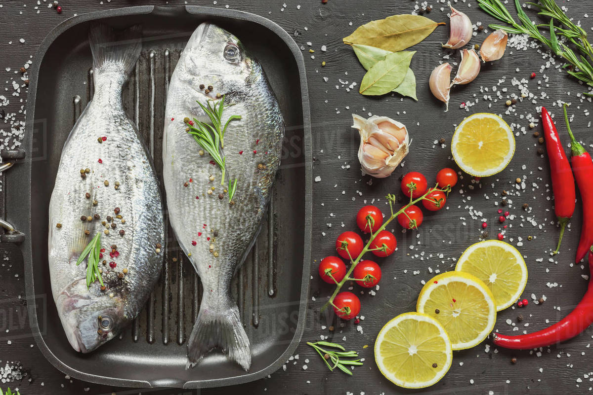 elevated view of uncooked fish near ingredients on black table Stock
