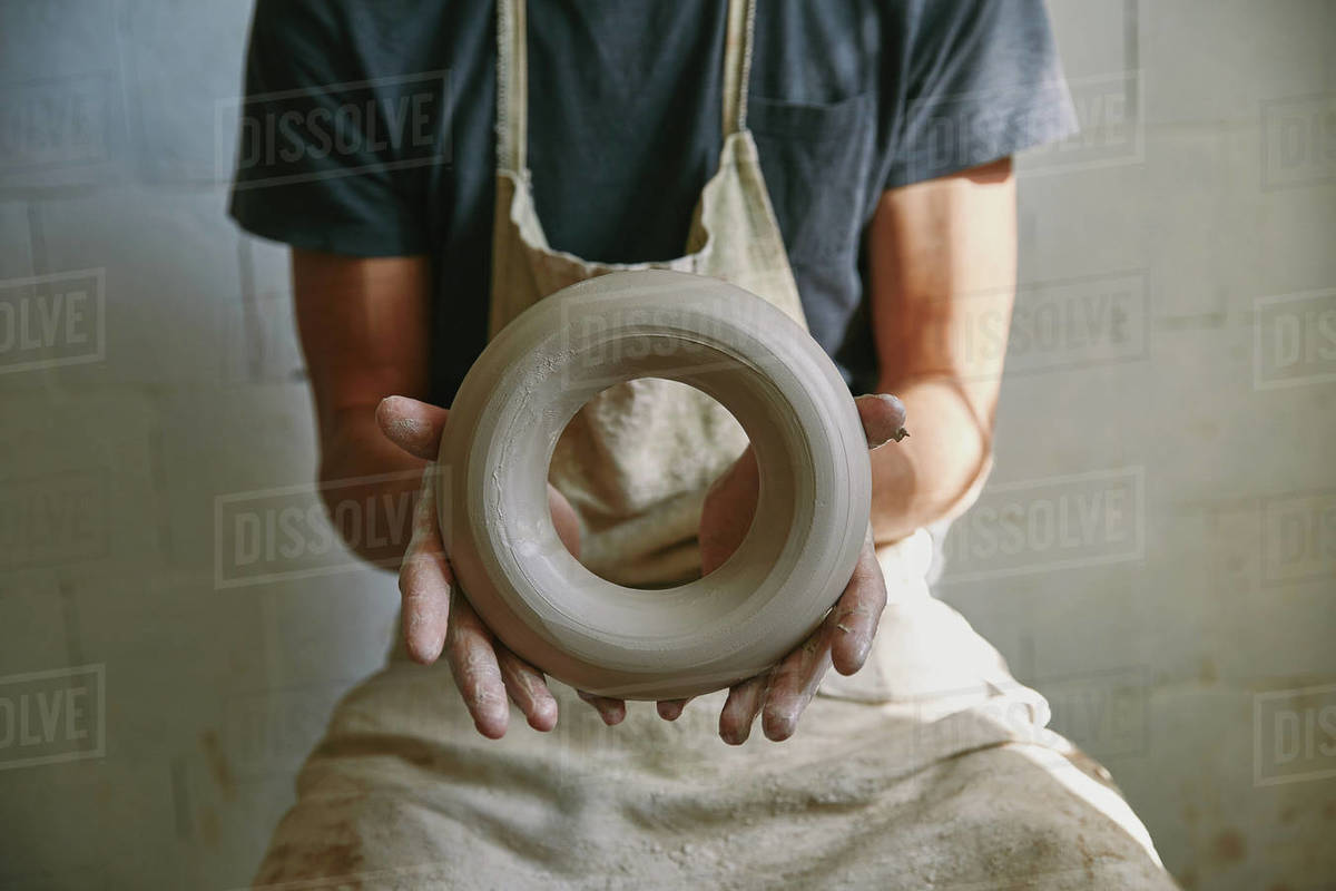 selective focus of professional potter in apron holding clay at pottery