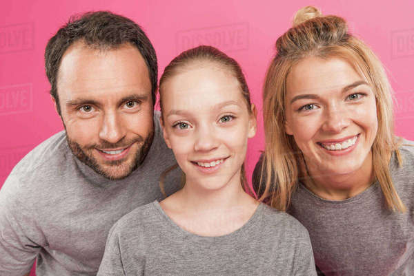Beautiful mother and father with happy daughter, isolated on pink ...