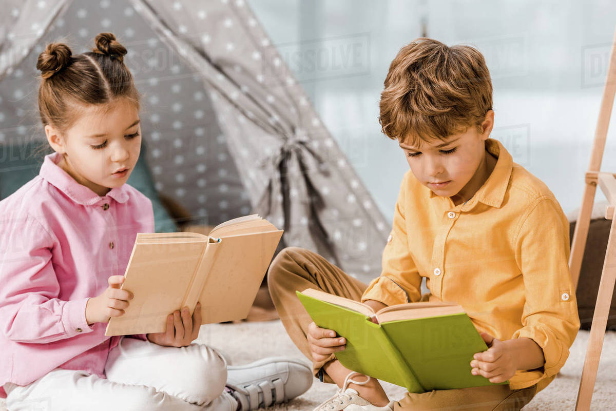 Cute focused children sitting on carpet and reading books together