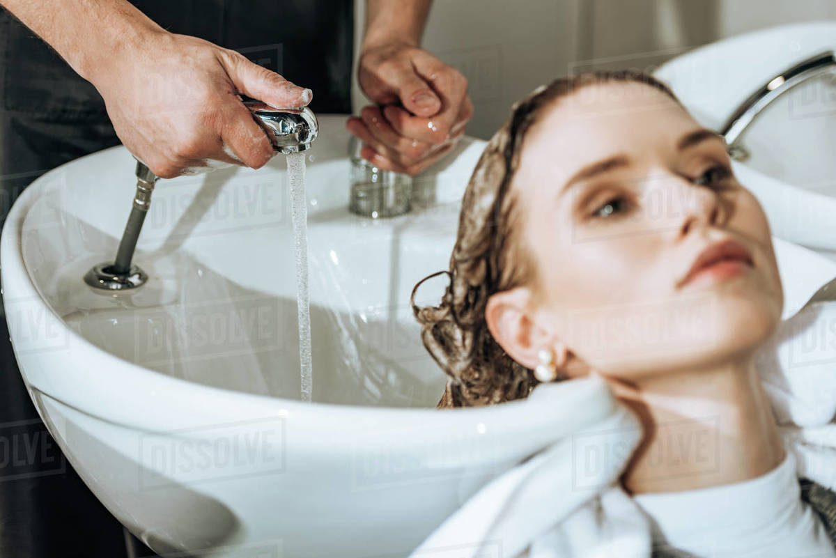 cropped shot of hairdresser checking water and washing hair to young woman in beauty salon