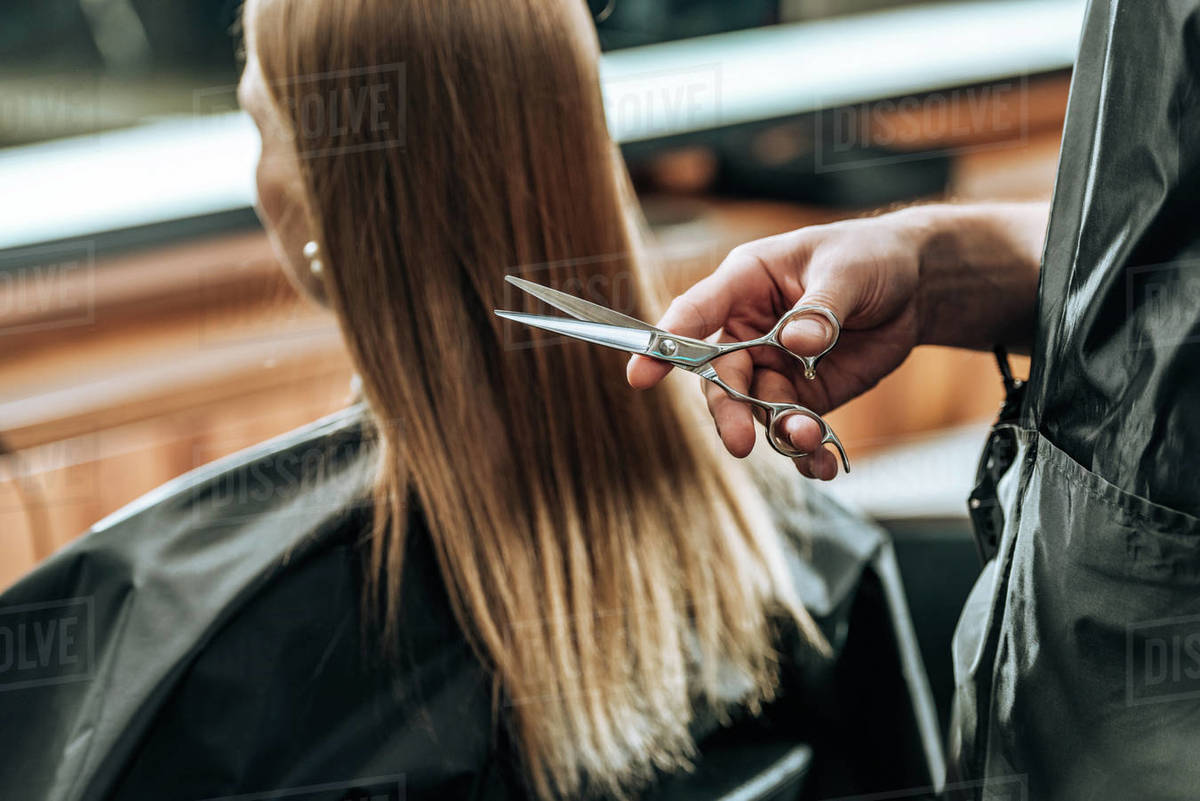 cropped shot of hairdresser holding scissors and young woman visiting