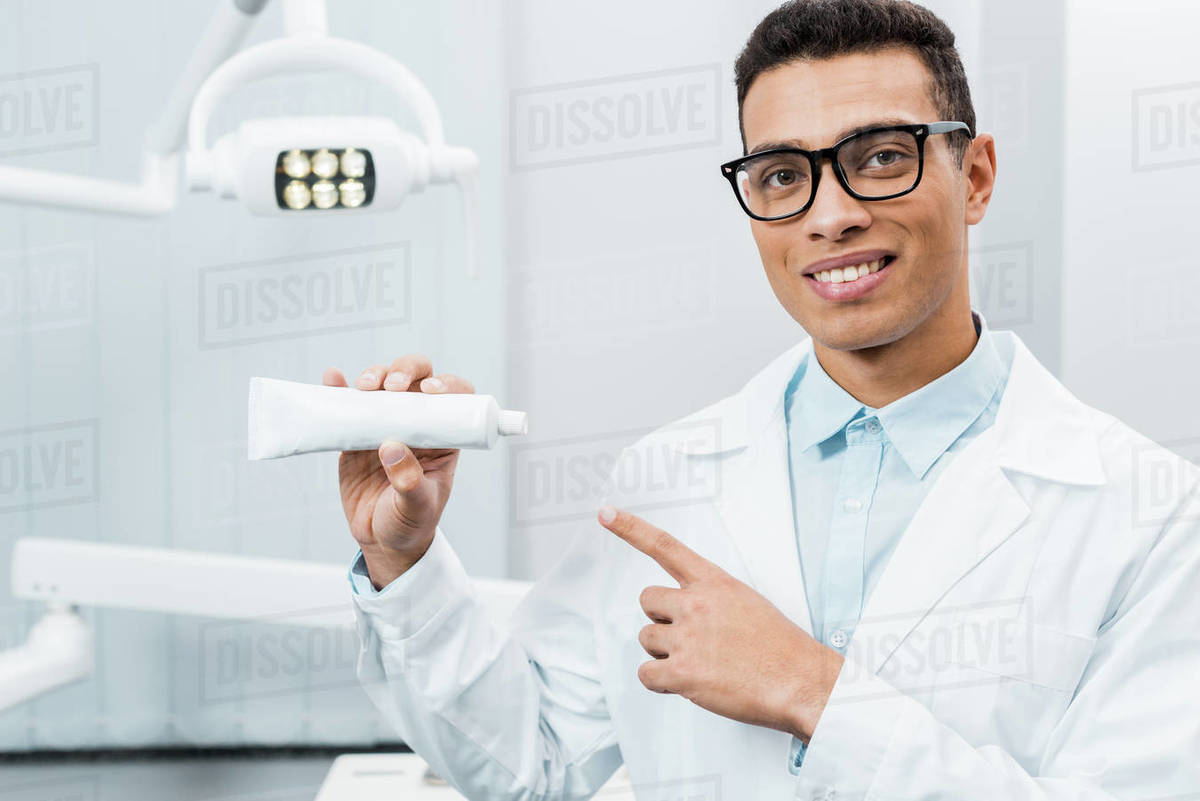 Handsome african american doctor showing toothpaste in dental clinic Stock Photo Dissolve