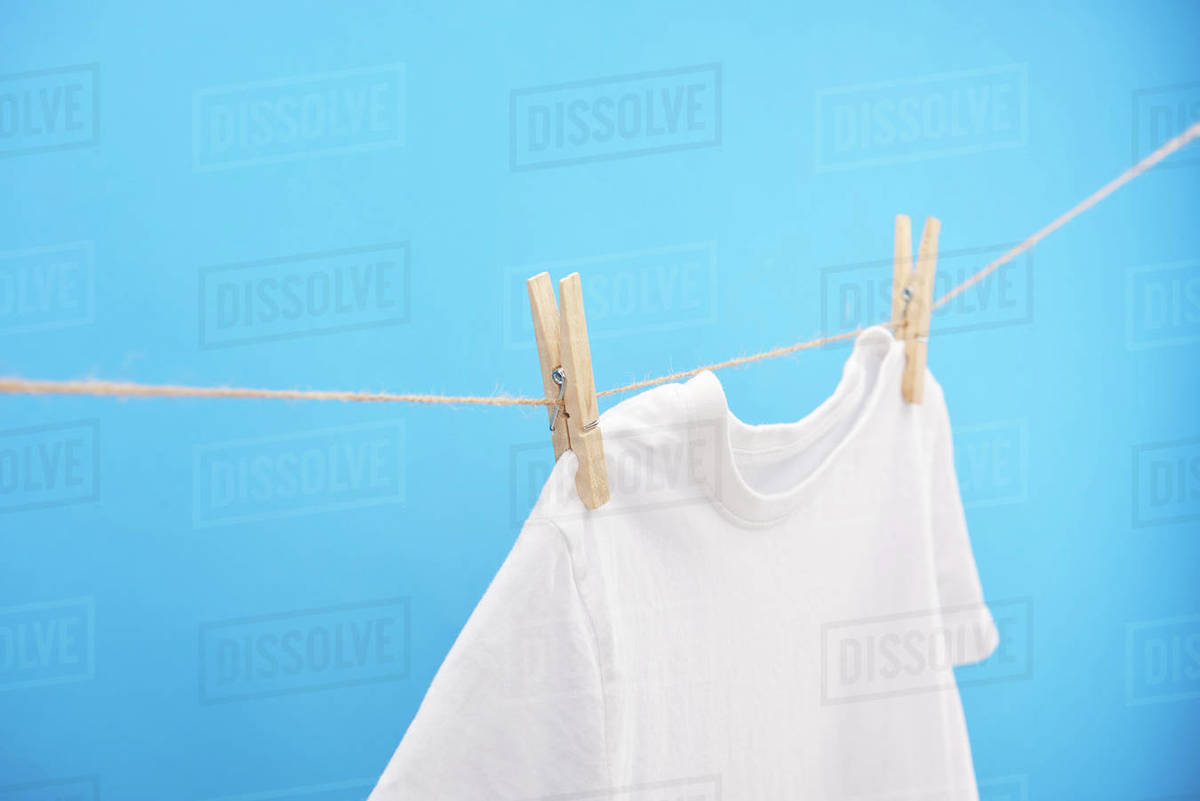 Clean white tshirt with clothespins hanging on rope isolated on blue