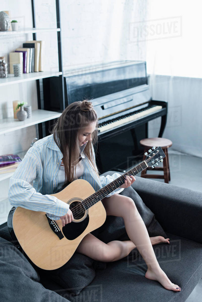 Attractive musician sitting on couch and playing acoustic guitar in