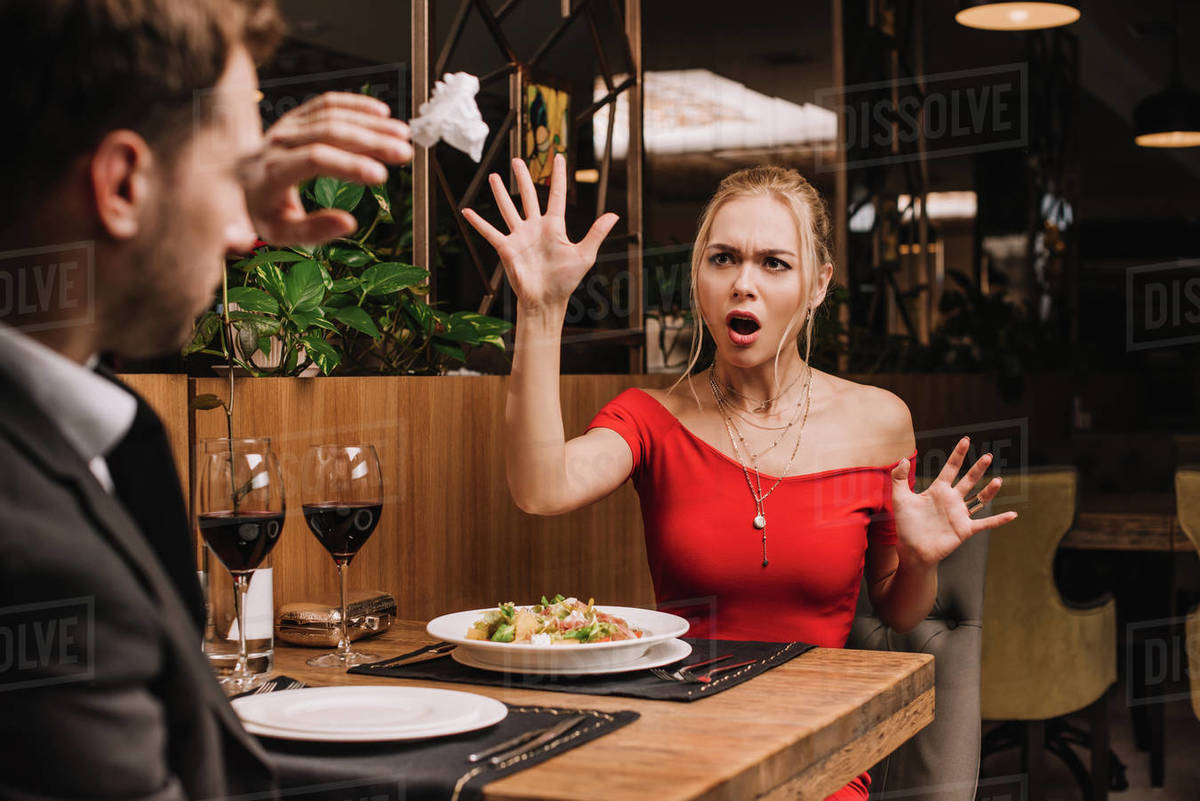 Shocked woman throwing napkin in boyfriend in restaurant Stock Photo