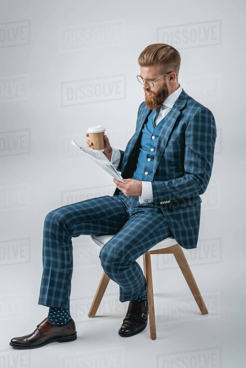 stylish man in suit with coffee to go reading newspaper while sitting ...