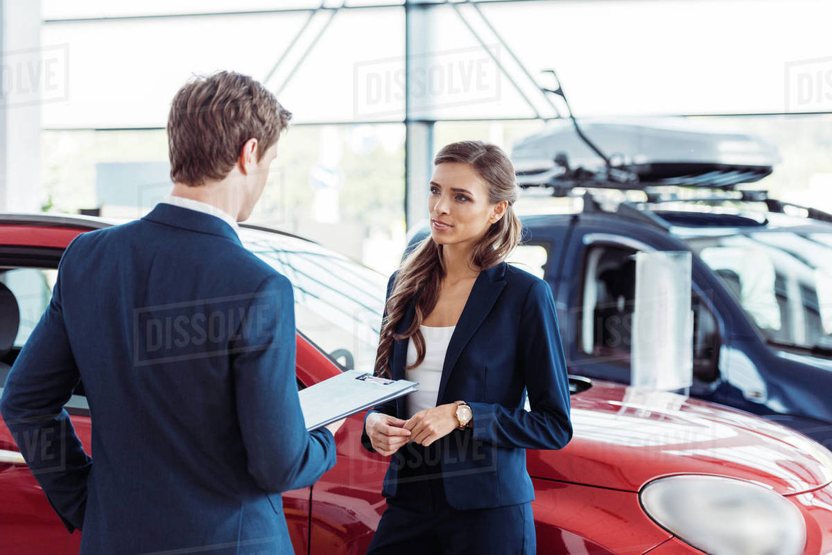 Female and male managers of car showroom standing and talking about
