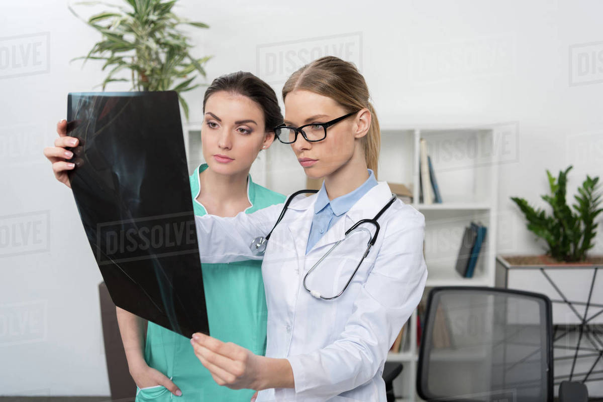 Serious doctor in eyeglasses and nurse examining xray image in