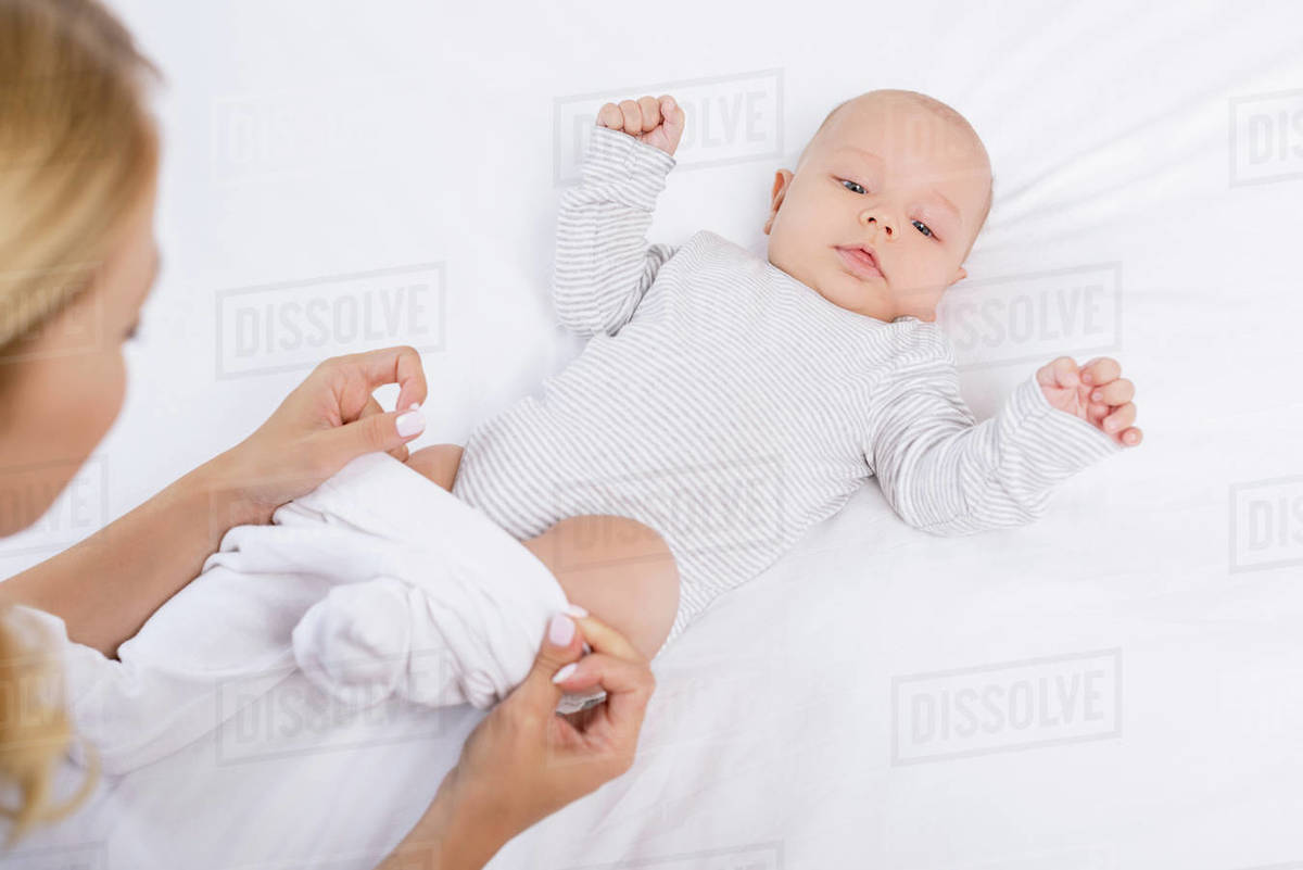 Cropped shot of mother dressing baby on bed Stock Photo Dissolve