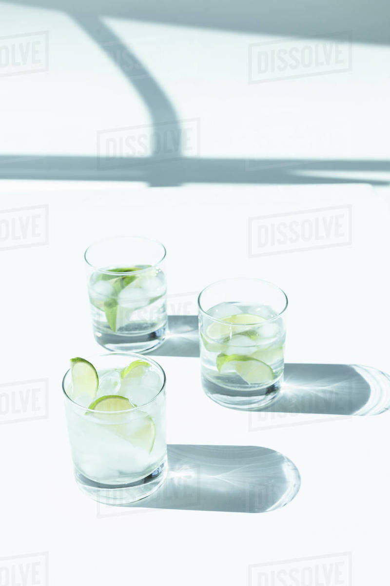 Closeup view of gin tonic cocktail with ice cubes in glasses and shadows on white Stock Photo
