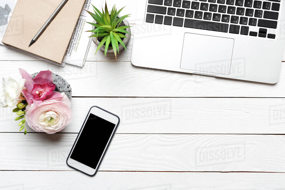Top view of laptop, smartphone and beautiful flowers in vase on desk