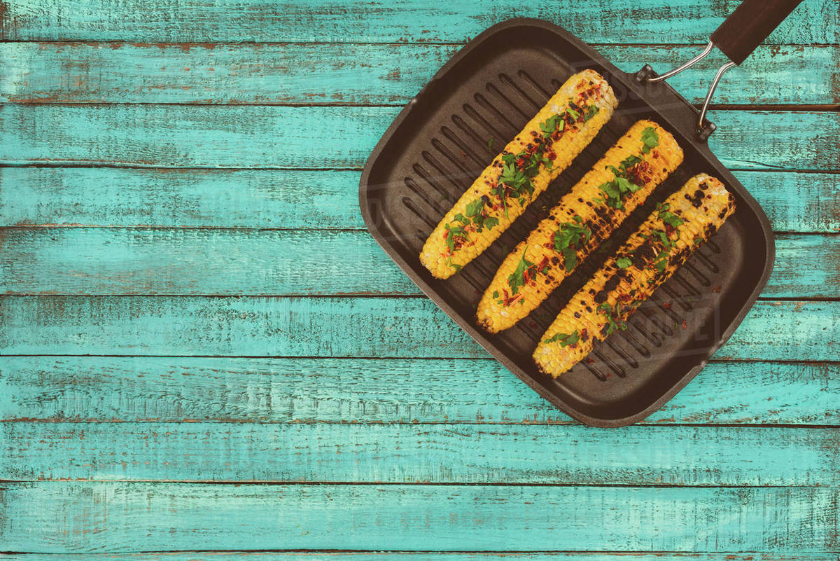 top view of roasted corn on grill pan and on blue wooden table Stock