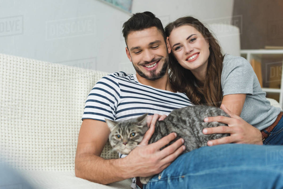 Happy Young Couple With Cute Tabby Cat Sitting On Couch Stock