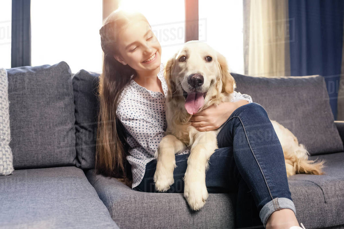 Teenager girl hugging golden retriever dog on sofa at home