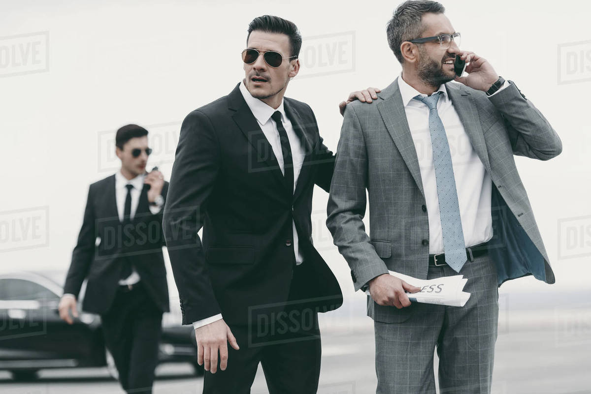 Businessman walking with two bodyguards and talking by smartphone