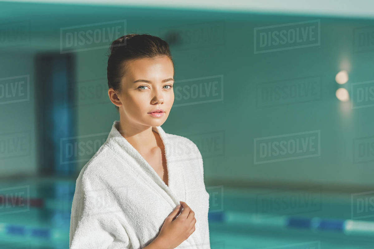 Beautiful young woman in bathrobe in front of swimming pool at spa