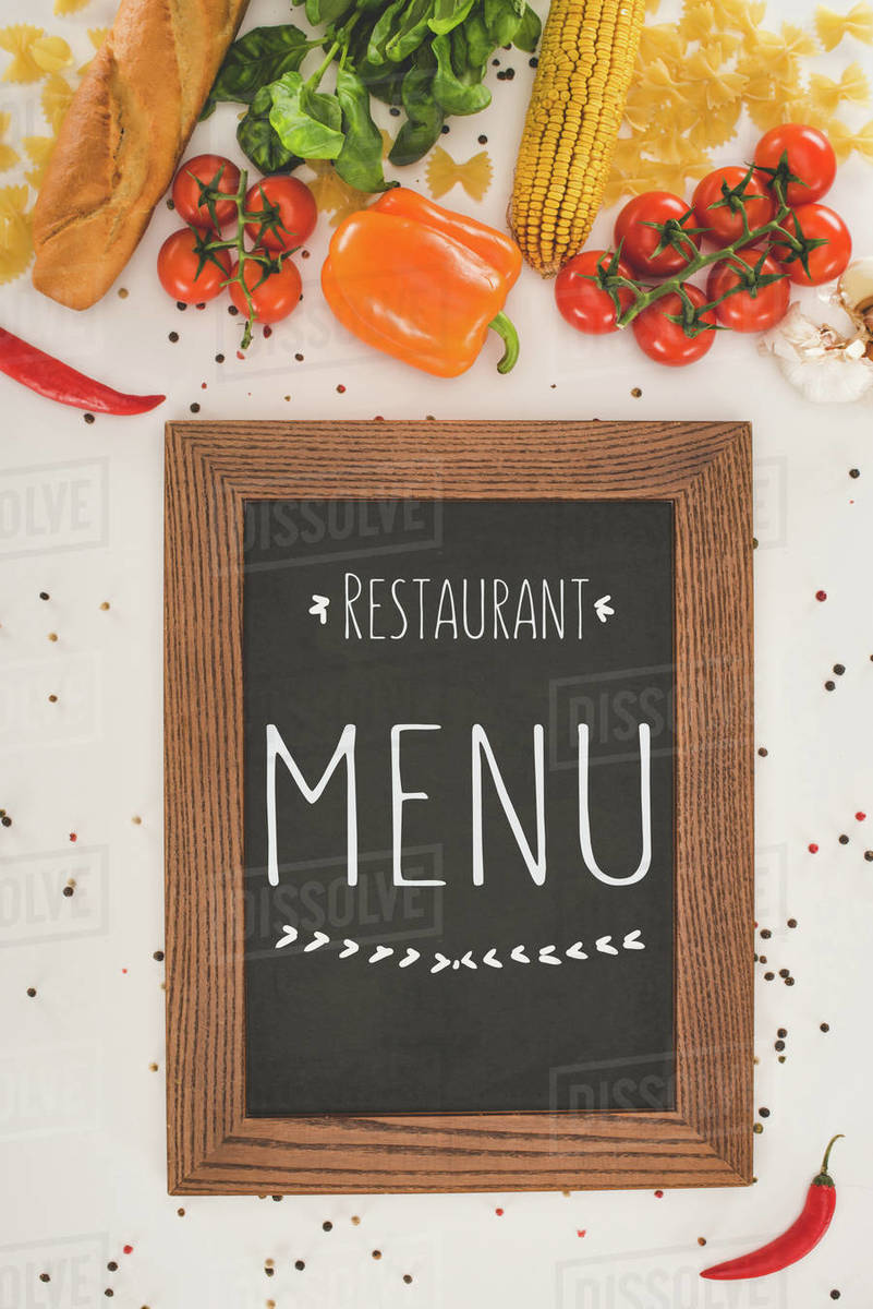 Top view of restaurant menu in wooden frame and fresh vegetables on