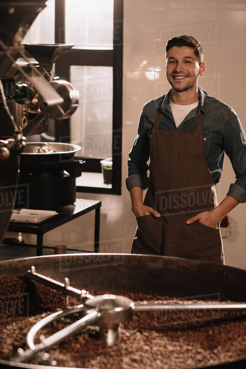 Portrait of smiling coffee roaster standing at roasting machine and looking at camera Stock