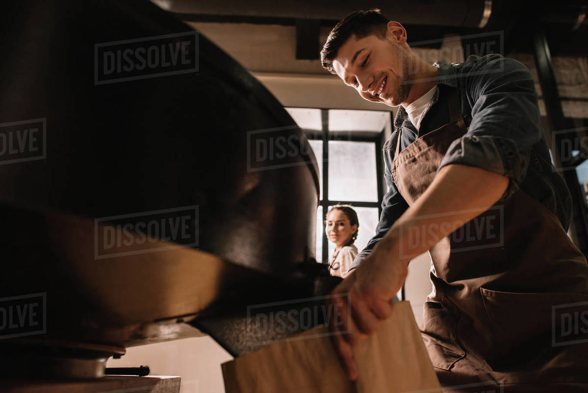 Coffee roaster roasting coffee beans in roasting machine with colleague