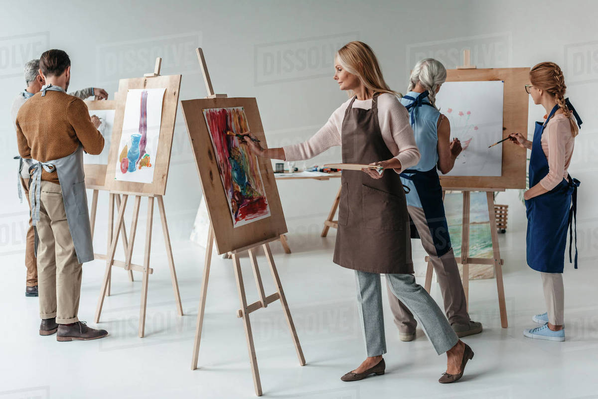 group of male and female adult students in aprons painting together on