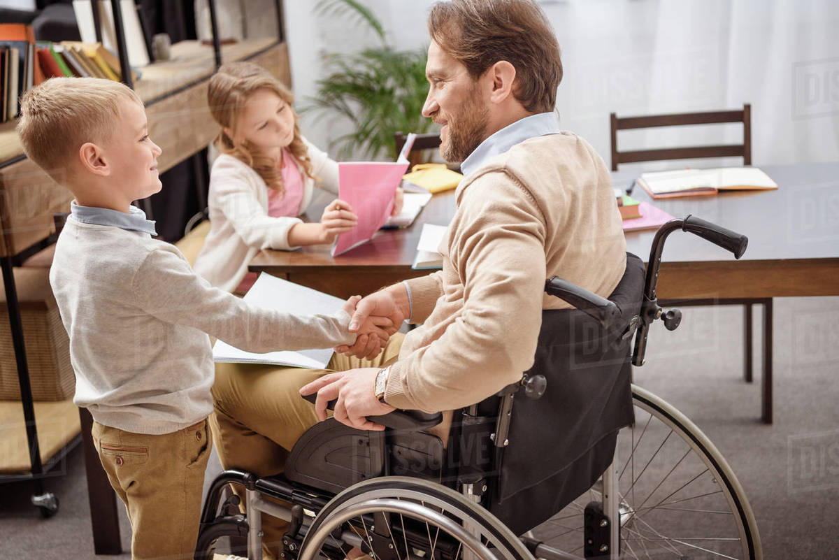 happy father on wheelchair and son shaking hands Stock Photo Dissolve
