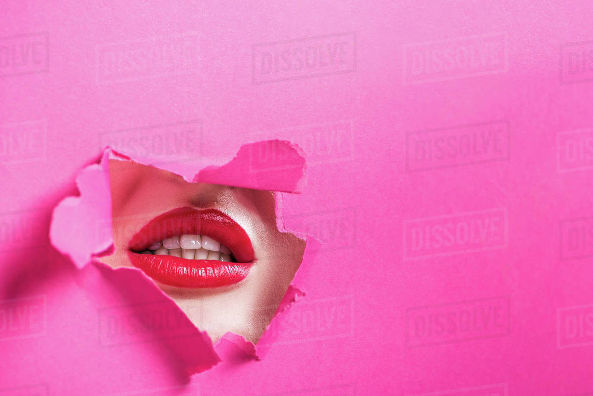 Cropped image of seductive girl showing lips in hole in pink paper ...