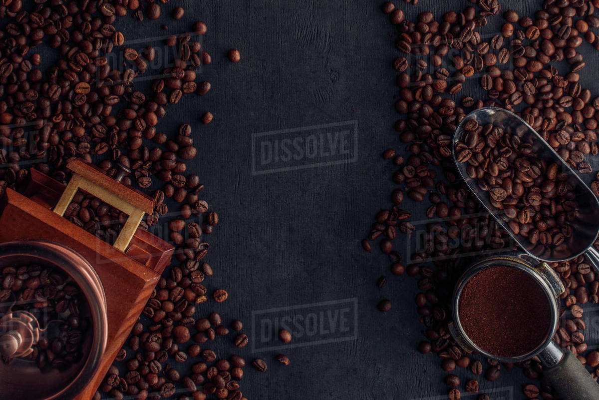 Top view of roasted coffee beans, coffee grinder and scoop on black