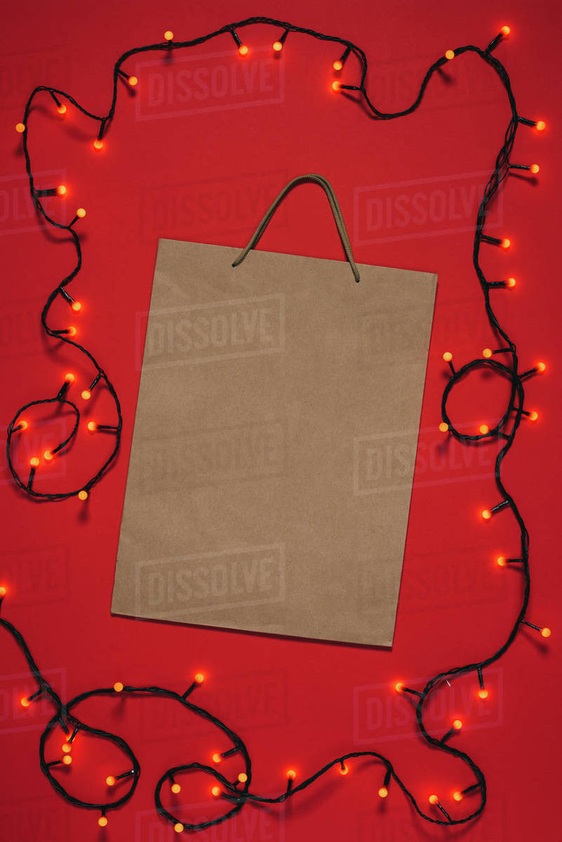 Top view of empty paper bag and Christmas lights isolated on red