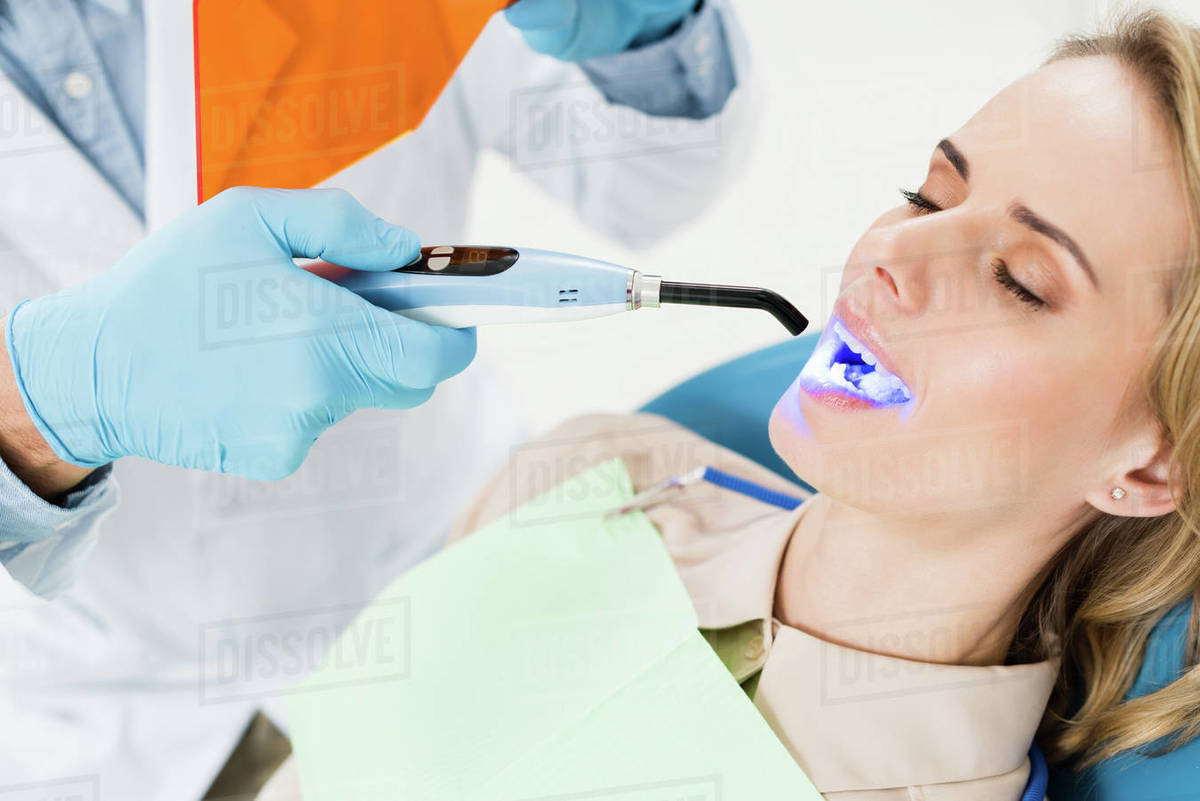 Dentist using uv lamp to treat patient teeth in modern dental clinic