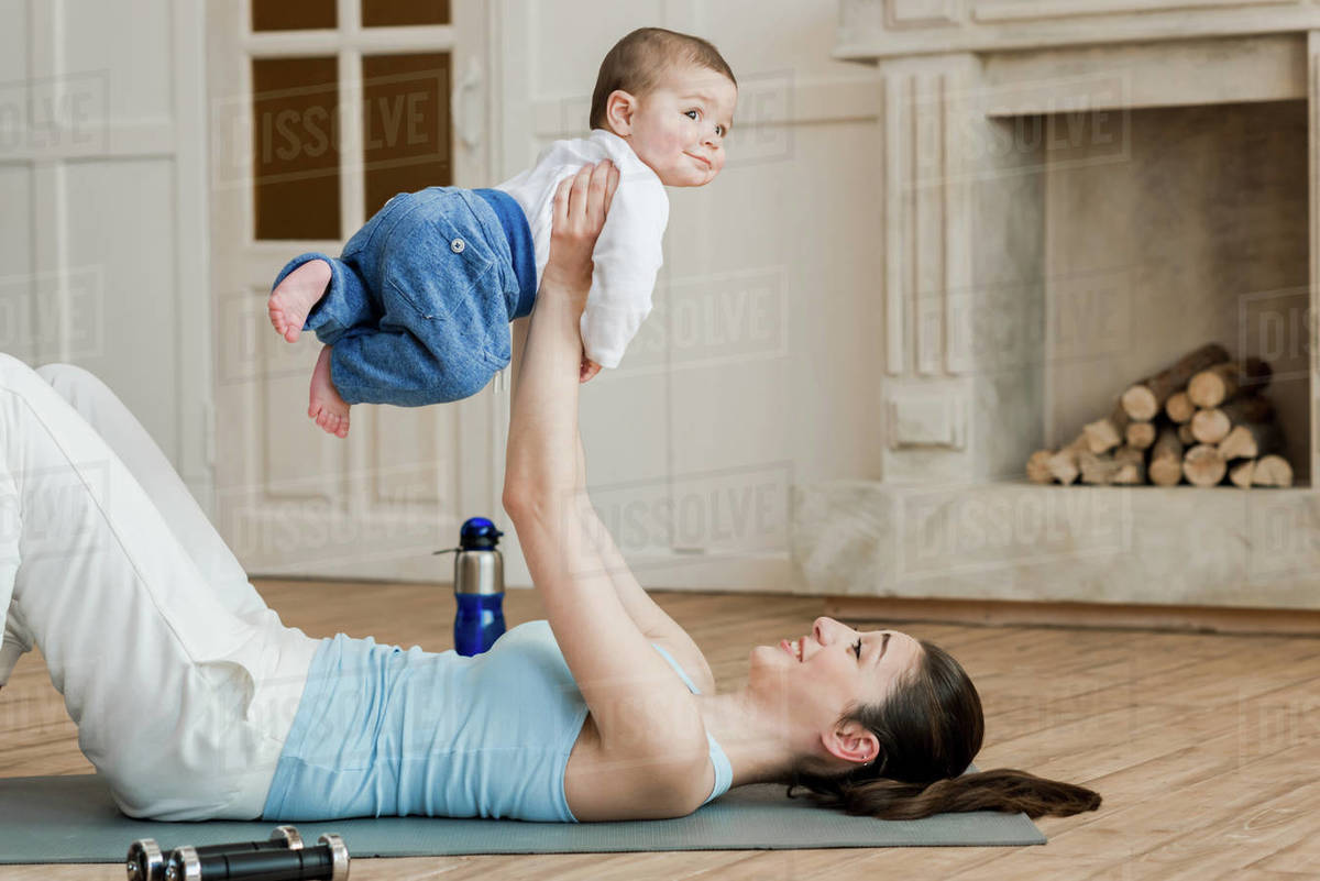 Side view of woman lying on yoga mat and playing with baby after