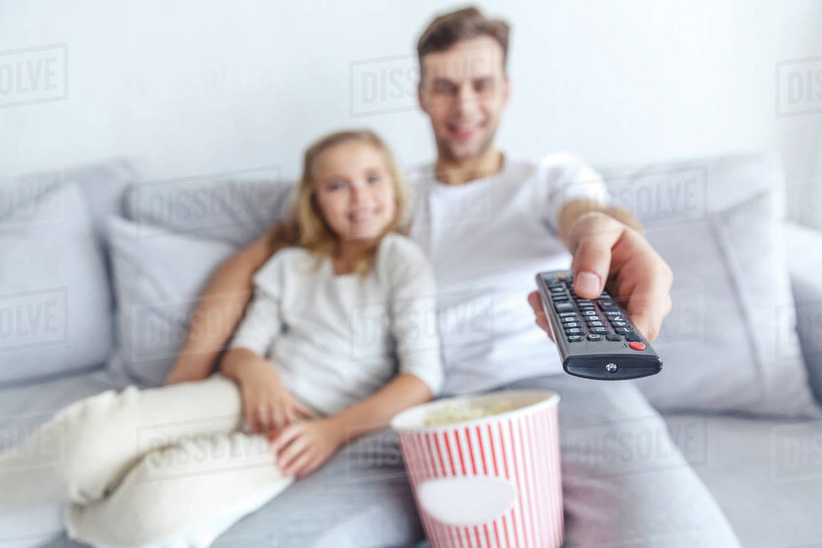 Close-up shot of father and daughter using tv remote control at home ...