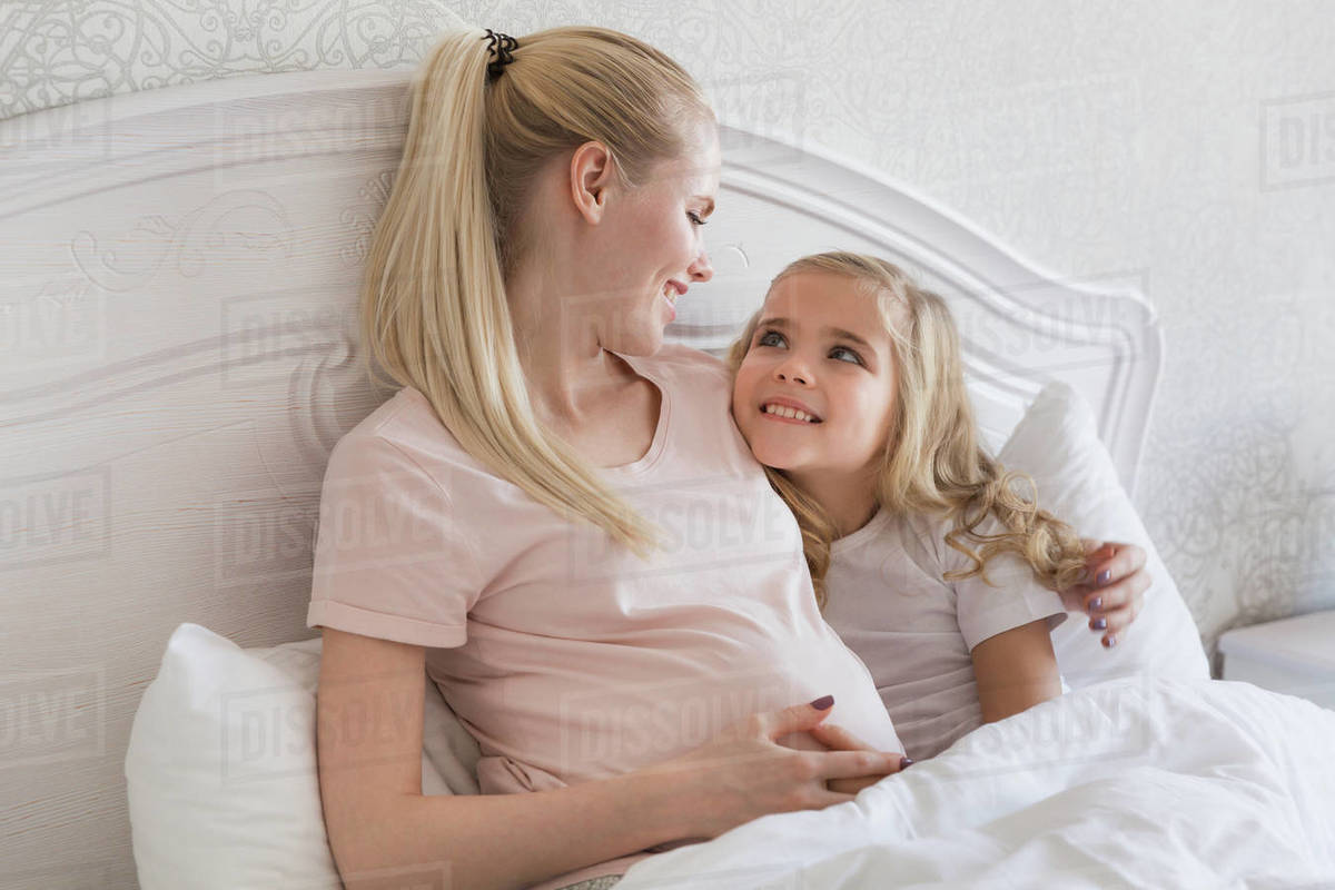 Smiling pregnant mother and daughter lying in bed Stock Photo Dissolve