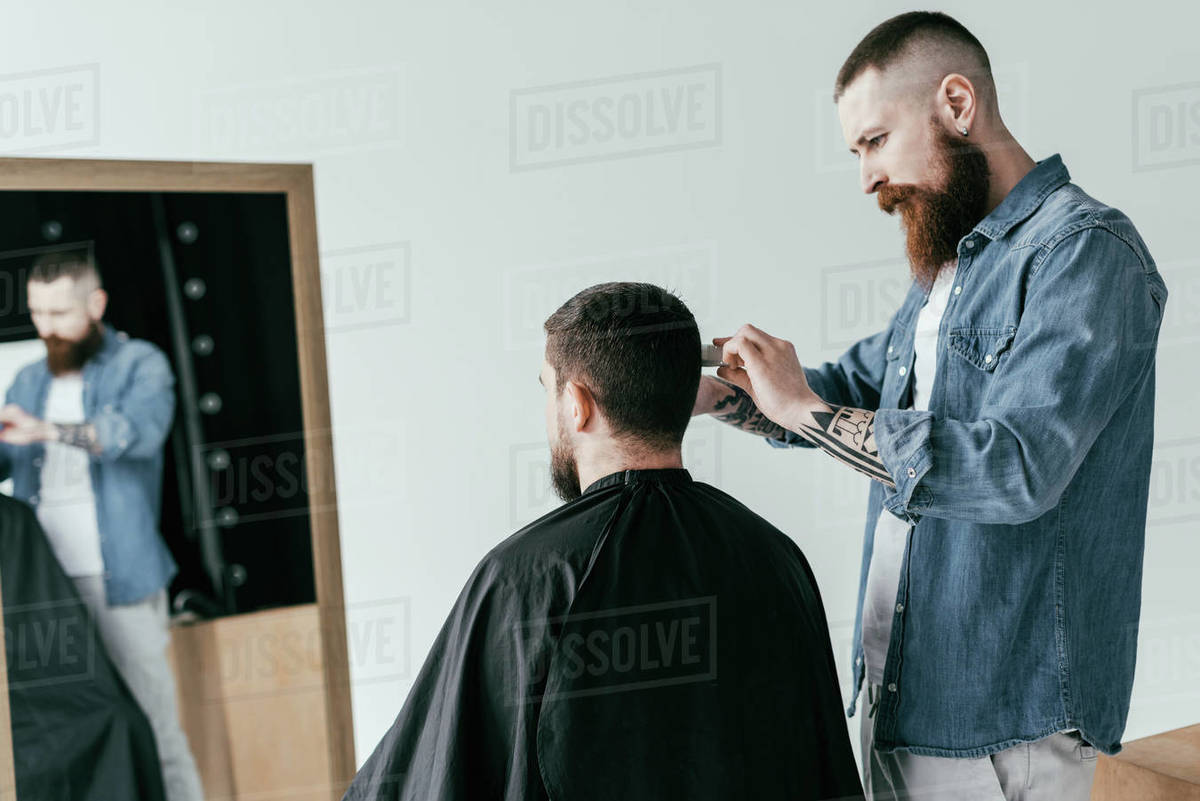 barber cutting customer hair in front of mirror at isolated