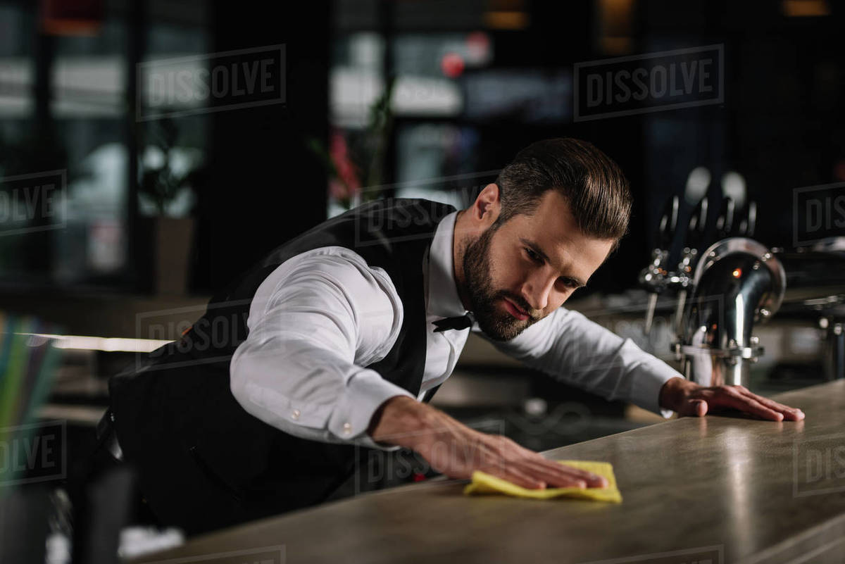 Handsome bartender cleaning bar counter in pub Stock Photo Dissolve