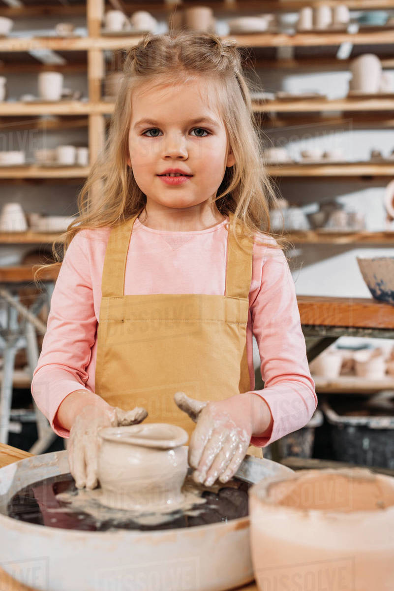 Little child making ceramic pot with clay on pottery wheel in