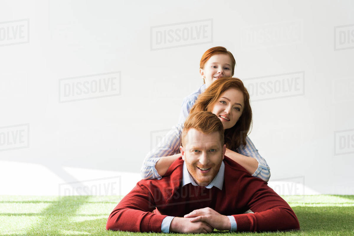 Happy Red Haired Family With One Kid Lying Together On Grass And