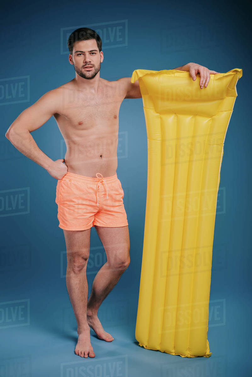Handsome young man in shorts standing with swimming mattress and