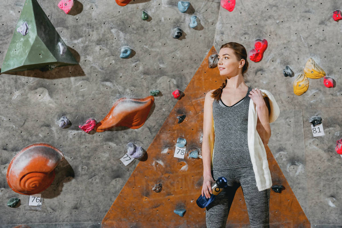 Halflength shot of a young woman in sportive attire posing in front of climbing wall Stock
