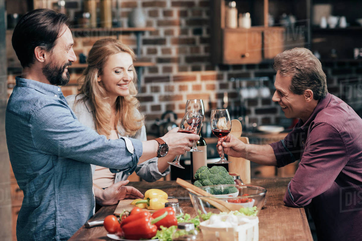 Smiling Caucasian friends drinking wine while cooking dinner Stock