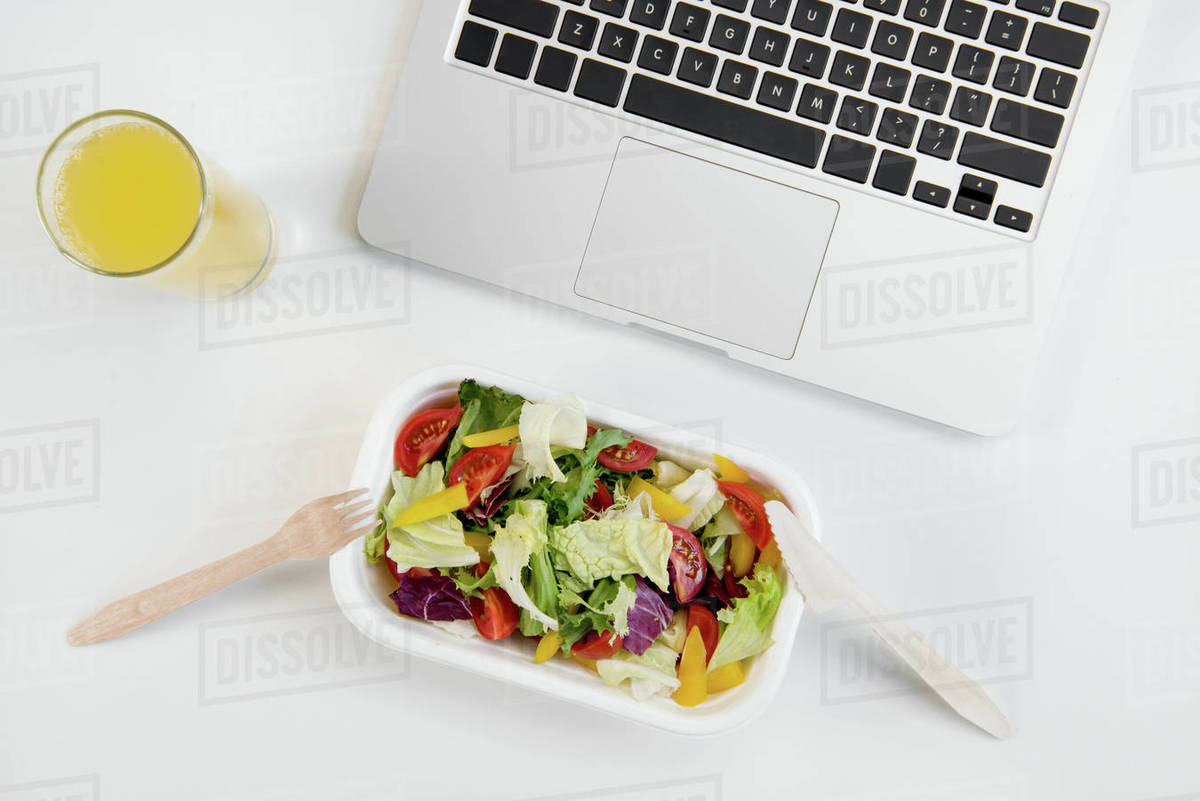 Top view of laptop, orange juice in glass and fresh salad in lunch box