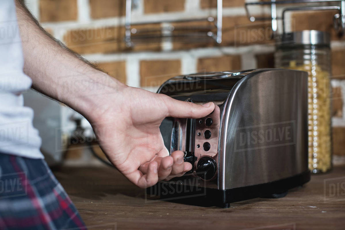 Cropped shot of man turning on toaster while preparing toasts at