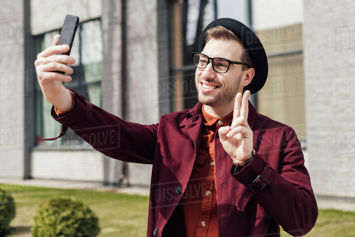 Handsome cheerful man showing peace symbol and taking selfie on smartphone Royalty-free stock photo