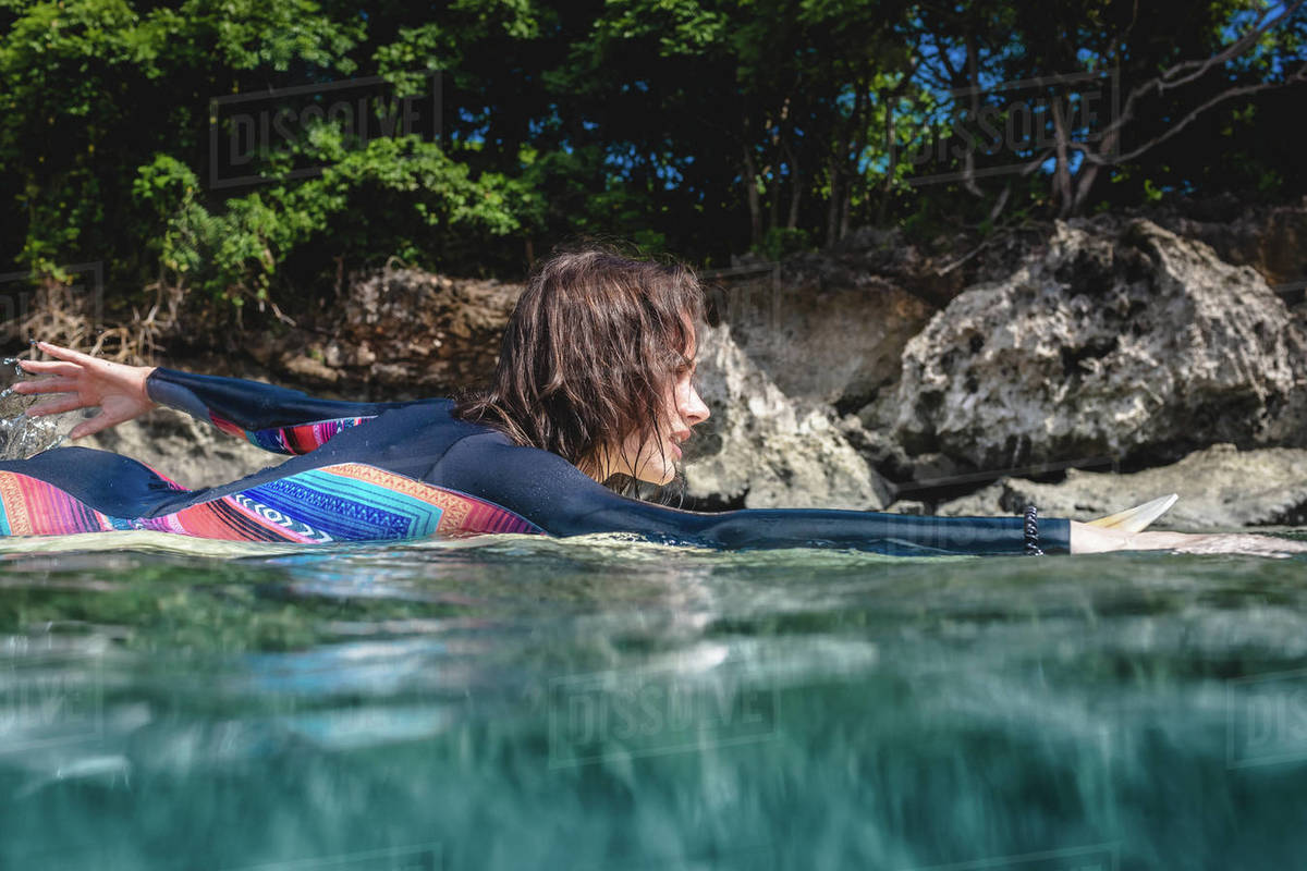 Side view of young sportswoman in wetsuit on surfing board in ocean at