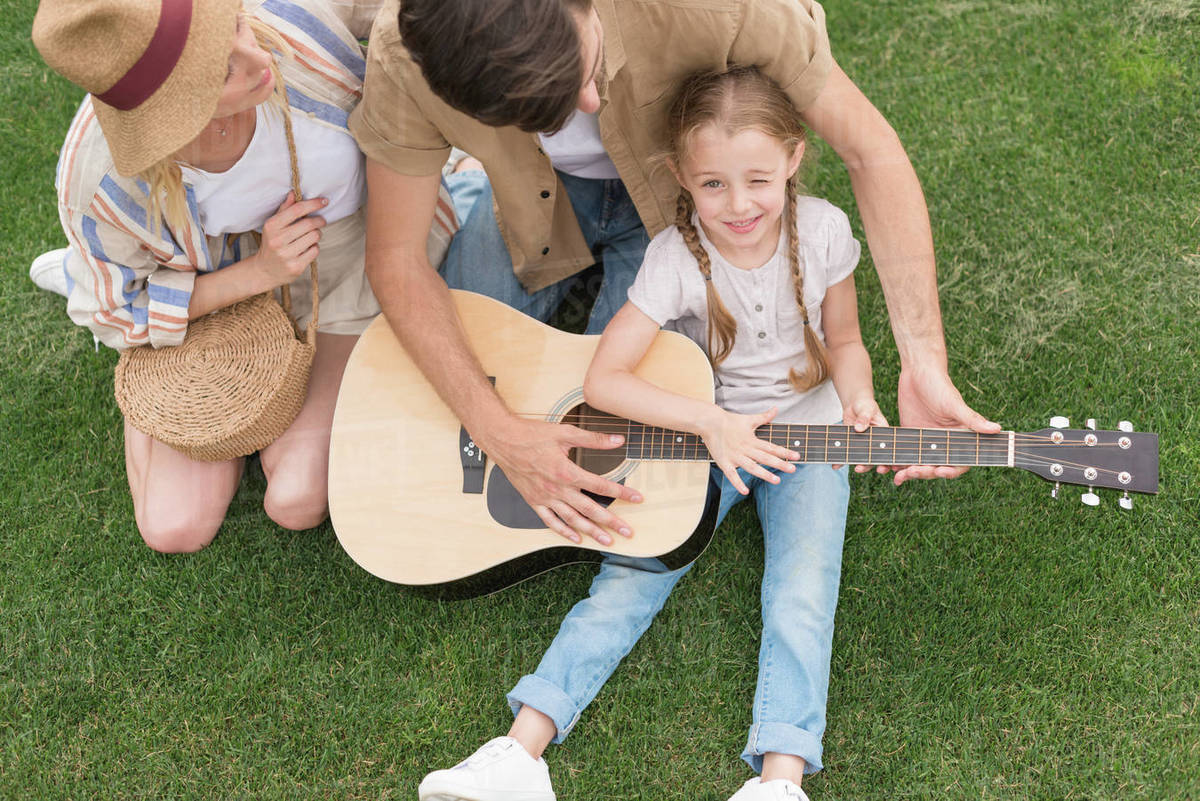 Overhead view of family with one child playing acoustic guitar on meadow Stock Photo Dissolve