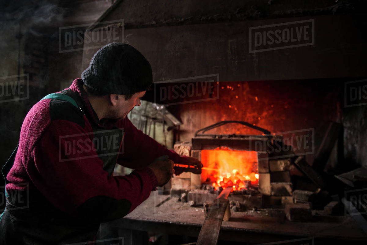 Blacksmith stirring coals in burning fire in his Stock Photo