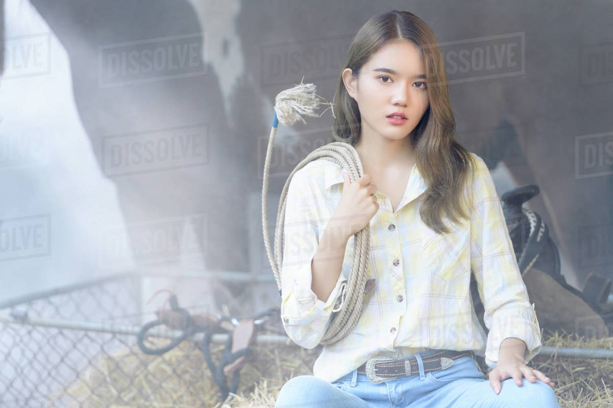 Woman sitting in a stable with a lasso rope in front of a horse ...