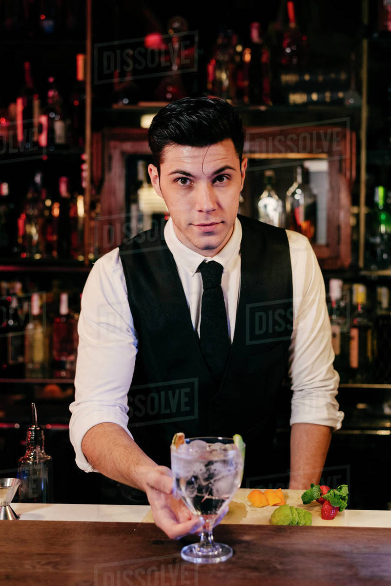 Young elegant barman working behind a bar counter mixing drinks with